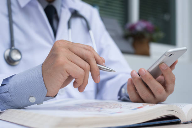 doctor using smartphone and reading book - medical student healthcare and medicine book education imagens e fotografias de stock