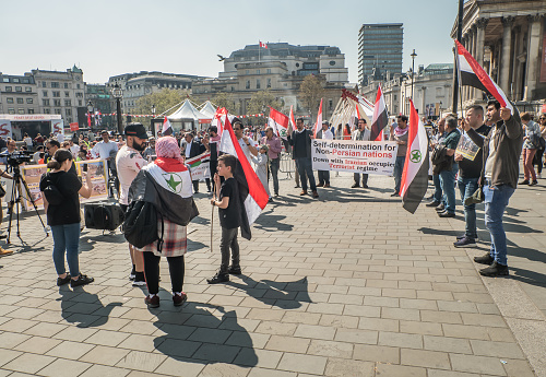 London, United Kingdom - Apr 19, 2019 : View of people with placards and Syrian flag on global strike for down with iranian occupied terrorist regime at Trafalgar Square. Selective focus.
