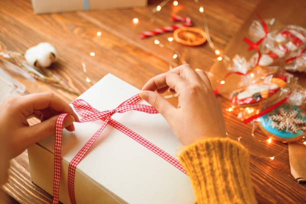 istock Girl's hands tie red ribbon bow on white gift box. 1335995727