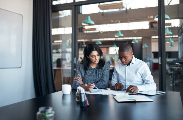 Shot of a businessman and businesswoman going over paperwork in a modern office Financial literacy is the surefire way for a company to grow financial literacy stock pictures, royalty-free photos & images