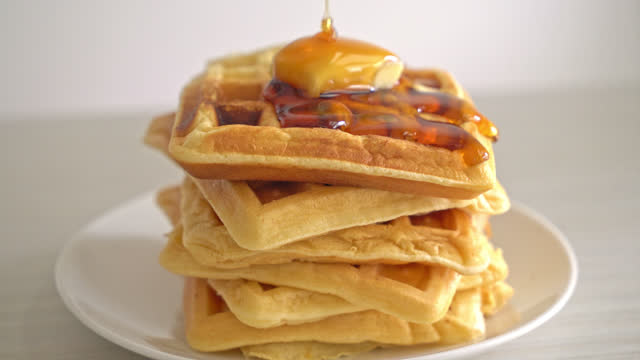 pouring honey or maple syrup on stack of waffles