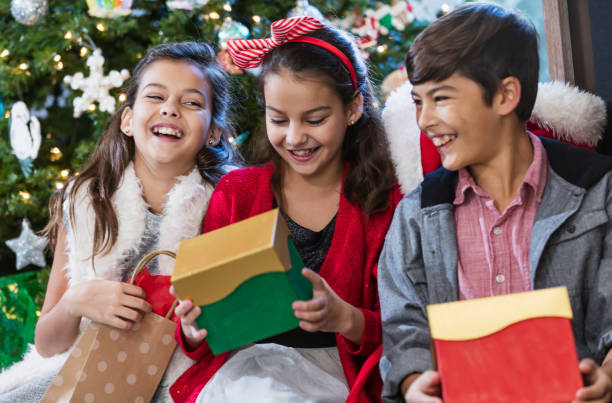 Children opening Christmas gifts Three children sitting in front of a Christmas tree opening their presents. They are siblings. The girls are identical twins, 11 years old. Their brother is 13 years old. florida christmas stock pictures, royalty-free photos & images