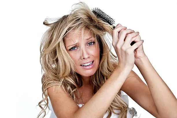 Woman with upset expression trying to get a brush out of her hair 