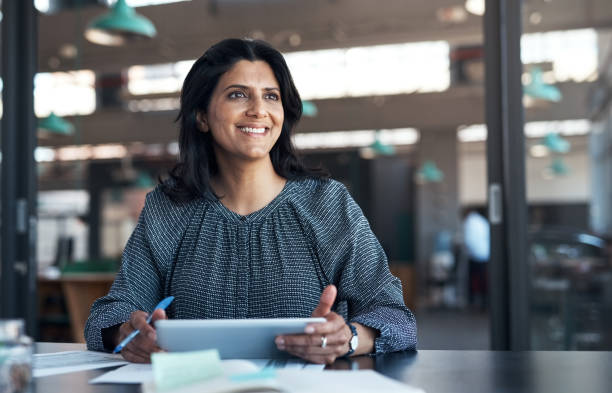 aufnahme einer reifen geschäftsfrau, die ein digitales tablet verwendet und in einem modernen büro papierkram durchläuft - thinking women businesswoman business person stock-fotos und bilder