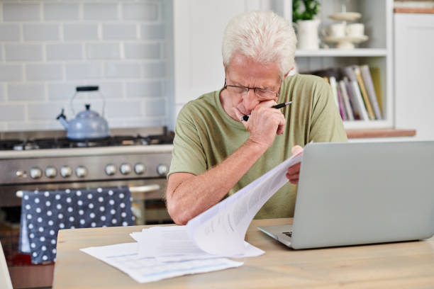 istock Shot of a senior man using a laptop and and going through paperwork at home 1336018655