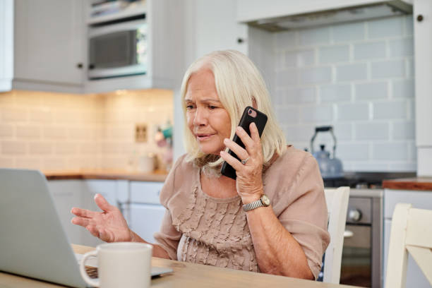 Shot of a senior woman looking angry while using a smartphone and laptop at home stock photo