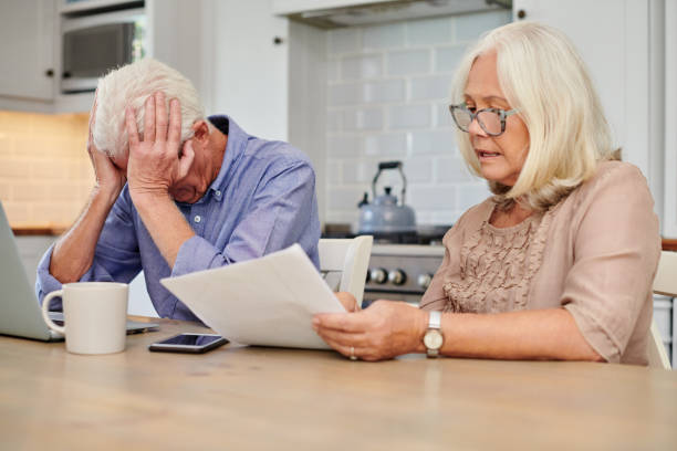 aufnahme eines älteren paares, das unglücklich aussieht, während es zu hause papierkram durchmacht - couple senior adult sadness emotional stress stock-fotos und bilder