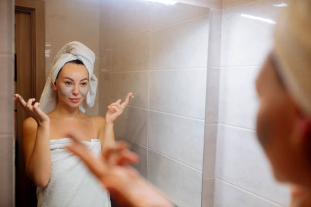 spa i kosmetologia. pielęgnacja skóry twarzy w domu. dziewczyna w łazience nakłada kremową maskę na twarz - clear sky human skin towel spa treatment zdjęcia i obrazy z banku zdjęć