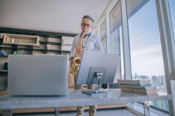 istock asian chinesse active senior man artist playing saxophone and showing it to his student using laptop at apartment living room in city live streaming 1336021919