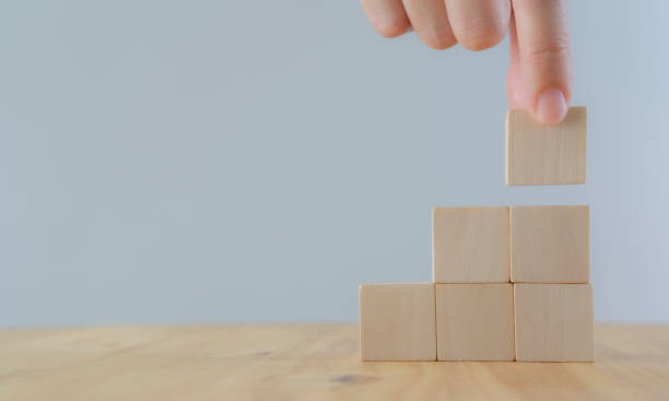 istock Business growth and management concept. Stack wood cubes on light background. Hand arranging wood cube stacking as stair step shape, mock up for create symbol or logo. Copy space. 1336021983