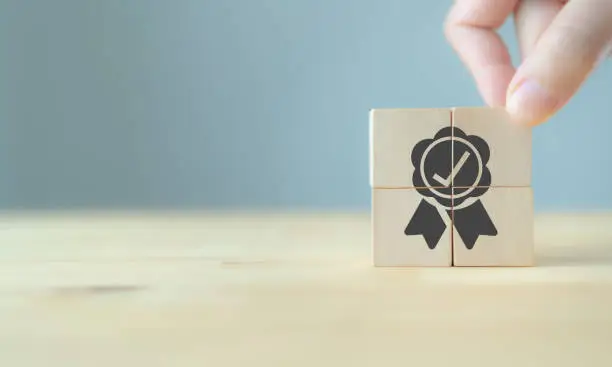 Photo of Quality warranty concept. Man's hand puts the wooden cubes with quality warranty icon on wooden cubes with grey background. Used for banner and advertising product and service quality commitment.