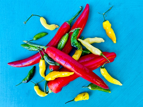 Horizontal high angle closeup photo of a pile of vibrant ripe chillies on a turquoise painted table top