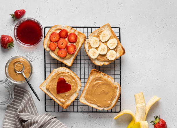 set di panini tostati al burro di arachidi su rack di raffreddamento. burro di arachidi e marmellata di fragole, fette di banana e strwaberry fresco. gustosa colazione sana. vista dall'alto del tavolo. - heart shape snack dessert symbol foto e immagini stock