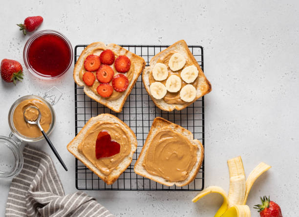 set of peanut butter toasted sandwiches on cooling rack. peanut butter and strawberry jam, banana slices and fresh strwaberry. tasty healthy breakfast. table top view. - peanutbutter bildbanksfoton och bilder