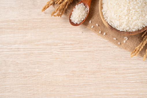 White raw rice in a bowl with the ear on the wooden table background.