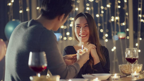 Caring boyfriend celebrating his girlfriend's birthday Cheerful young woman blows the candle on cupcake brought by her boyfriend candle light dinner stock pictures, royalty-free photos & images
