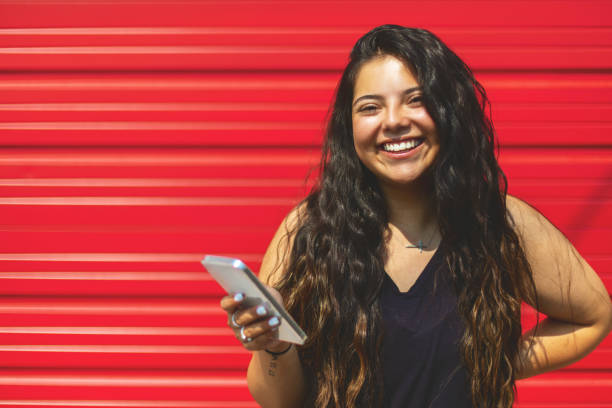istock Hispanic Native American Generation Z Female Using Smart Phone Technology Standing In Front of Red Garage Door Urban Photo Series 1336040120