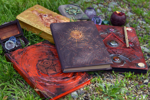 Pile of witch grimoire book of magic spells and burning candle in the garden. stock photo