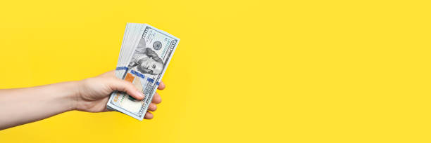 istock Hand holding a big stack of banknotes isolated on yellow background. Wealth or loan concept. Long Banner with copy space. 1336045165
