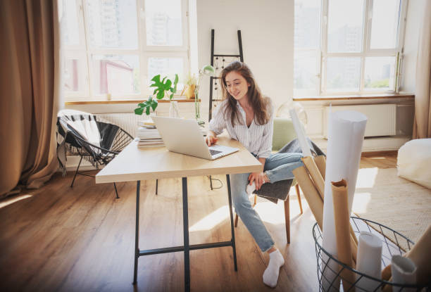 istock Beautiful happy young woman hipster designer working on a project using laptop and blueprints in rolls at home in apartment 1336049183