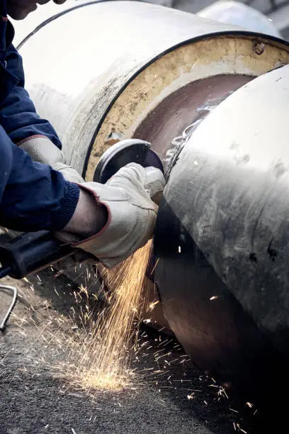 Construction worker cutting the metal pipe with a anglegrinder.
