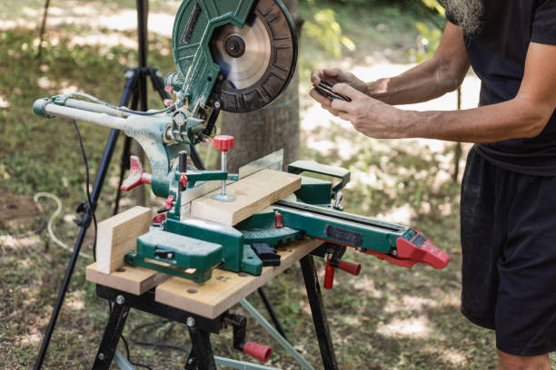 DIY woodworking, cutting wood plank, photographing DIY woodworking - man photographing wood plank on miter saw prior cross cutting,  using smartphone, obscured face, real people miter saw stock pictures, royalty-free photos & images