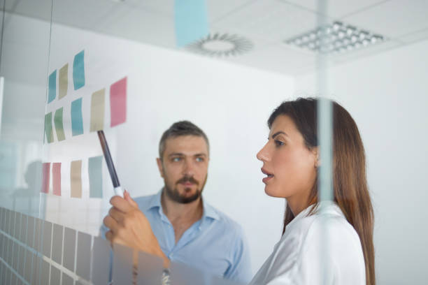 istock Two coworkers sharing ideas on sticky notes on glass wall 1336057022