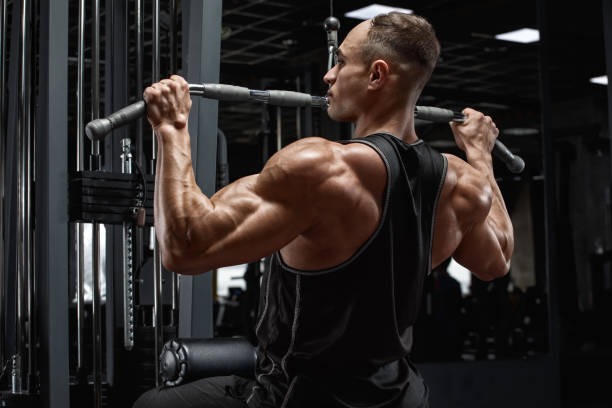 musculoso homem treino na academia, fazendo exercício para recuo lat recuo. forte visão traseira masculina - beautiful one person strength sensuality - fotografias e filmes do acervo