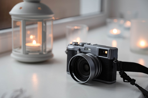 Close-up of vintage camera on white sill. Old fashion. Retro hipster photography. Burning candles on background. Hygge concept.