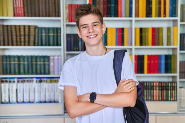 pojedynczy portret uśmiechniętego, pewnego siebie nastolatka studenta patrzącego na aparat w bibliotece - early teens zdjęcia i obrazy z banku zdjęć