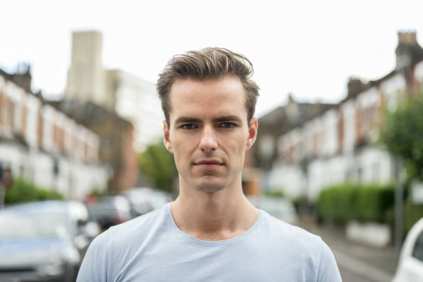 Portrait of young Caucasian man in light grey t-shirt Head and shoulders view of casually dressed man with short hair standing outdoors in residential neighborhood and looking at camera with serious expression. wandsworth photos stock pictures, royalty-free photos & images
