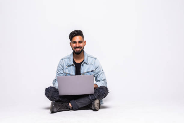 istock Handsome guy working on a laptop and sitting on a floor, isolated against white background 1336071373