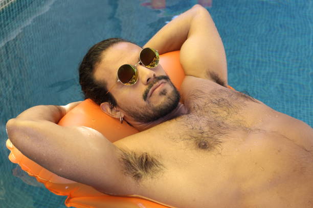 Attractive ethnic man floating in swimming pool Attractive ethnic man floating in swimming pool . gay long hair stock pictures, royalty-free photos & images