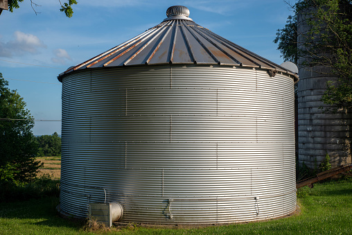 Green grass and blue sky surrounf a silver corrugated steel grain dryer, metal texture and good shape. No people with copy space.