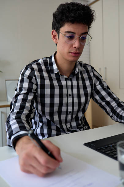 istock young man with glasses taking notes in front of laptop at home 1336075149