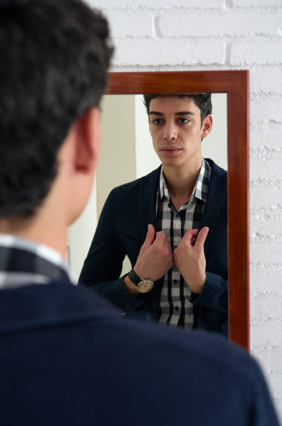 istock young man adjusting the jacket with both hands in front of the mirror on the wall 1336075272