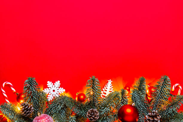 Two purple Christmas ornaments selectively focused and a red bead garland are reflected in a mirrored surface with bokeh lighting.