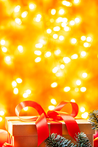 Close up of a brown Christmas present with red ribbon and Christmas decoration shot against defocused yellow Christmas lights. The composition is at the bottom of an horizontal frame leaving useful copy space for text and/or logo.