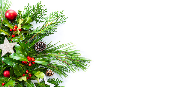 Christmas frame with green fir tree branches, mistletoe and red baubles decoration on white background. The composition is at the left of an horizontal frame leaving useful copy space for text and/or logo.