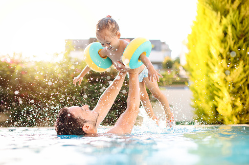 A young mother and her adorable baby are playing in the pool with water pistols, splashing water around.