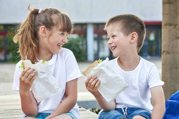 snack während des unterrichts. nahaufnahme von glücklichen kindern, die auf dem schulhof frühstücken. mahlzeiten für schüler während des unterrichts - junior school stock-fotos und bilder