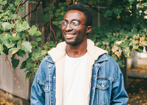 Portrait of happy smiling african man looking away wearing an eyeglasses in autumn city park
