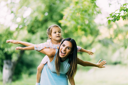 Cute young daughter on a piggy back ride with her mother.