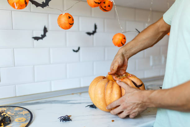 eine nahaufnahme der hand des mannes zieht samen und faseriges material aus einem kürbis, bevor sie für halloween schnitzt. jack-o-laterne. seitenansicht in der küche - photography close up side view halloween stock-fotos und bilder