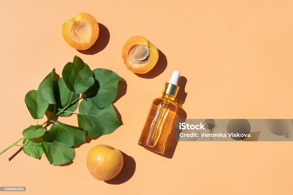 Serum or oil in glass bottle with fresh apricots fruit on pastel orange background. Serum or oil in glass bottle with fresh apricots fruit on pastel orange background. Natural cosmetic beauty product branding mock-up for brightening cream, body lotion, facial foam. Flat lay. Essential Oil Stock Photo