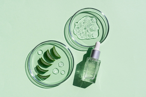 Flat lay of cosmetics serum and and laboratory glassware with fresh leaves of aloe vera on bright green background. Organic cosmetics. Top view flat lay, copy space. Cosmetics, SPA branding, mock-up.