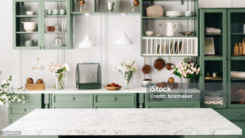 Countertop with green vintage kitchen furniture in blurred background Clean and empty marble countertop, green vintage kitchen furniture with lots of flowers and bowl of strawberries, pair of white hanging pendant lights, various crockery in blurred background Kitchen Stock Photo