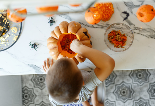 Halloween pumpkin cutting process, process of making Jack-o-lantern. Boy hands with knife, leftovers of pumpkin on the kitchen table.