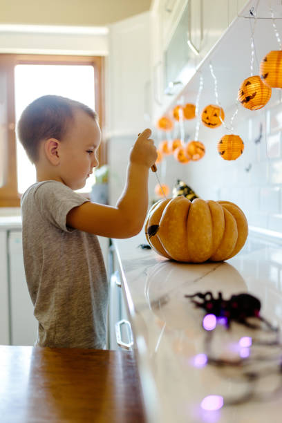 istock Halloween pumpkin cutting process, process of making Jack-o-lantern. Boy hands with knife, leftovers of pumpkin on the kitchen table 1336086016