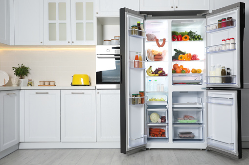 Unrecognizable Young Woman Opening Fridge In Kitchen And Looking Inside, Hungry Brunette Lady Standing Near Open Refrigerator At Home, Starving Female Checking Food Or Drinks, Free Space
